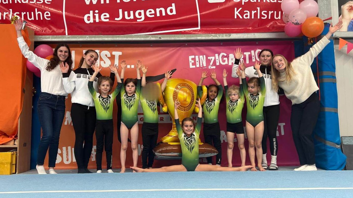 Turnerinnen, Trainerinnen und Kampfrichterinnen stehen vor einer bunten Wand und jubeln